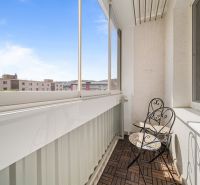 Zasklený balkon s dřevěným dekorem podlahy v 3-pokojovém bytě se stolem a židlemi.