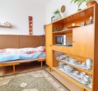 Pokoj v rodinném domě s postelí, retro nábytkem a poličkami s porcelánem.