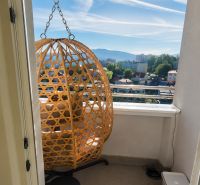 Balkon v 2-pokojovém bytě s ratanovým křeslem a výhledem na město.