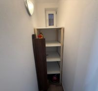 Spižírna v 2-pokojovém bytě s bílým regálem a drobnými předměty na poličkách.
