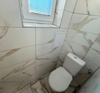 Koupelna v 2-pokojovém bytě s elegantními stěnovými dlaždicemi a malým oknem.