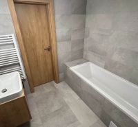 Koupelna v rekreačním apartmánu s vanou, umyvadlem a šedými obklady.