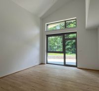 Interiér rekreačního apartmánu s velkým oknem a podlahou s dřevěným dekorem.
