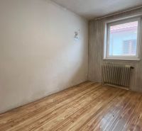 Pokoj s podlahou s dřevěným dekorem, radiátorem a tapetou v rodinném domě.