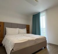 Rekreační apartmán s pohodlnou postelí, závěsy a podlahou s dřevěným dekorem.