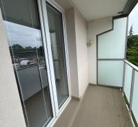 Balkon v 2-pokojovém bytě se skleněným zábradlím a dlaždicovou podlahou.