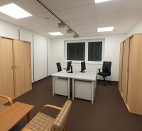 Kanceláře s počítači, kancelářskými židlemi a policemi, podlaha s dřevěným dekorem.