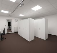 Kanceláře s pracovním stolem, židlí a skříňkami, podlaha s tmavým kobercem.