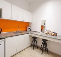 Kanceláře s kuchyňkou, bílými skříňkami, oranžovou stěnou a podlahou s dřevěným dekorem.