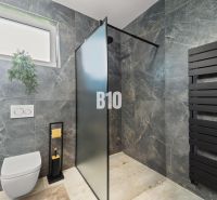 Koupelna v rodinném domě s černým radiátorem a sprchovým koutem.