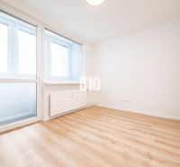 Prostorný pokoj v 3pokojovém bytě s velkými okny a podlahou s dřevěným dekorem.
