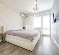 Ložnice s postelí, vzorovanou tapetou a podlahou s dřevěným dekorem v rodinném domě.