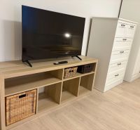 Televize na poličce s košíky, vedle komody a skříně, podlaha s dřevěným dekorem.
