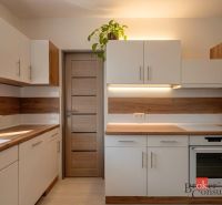 Kuchyně s podlahou s dřevěným dekorem, bílo-hnědé skříňky, rostlina na skříňce.