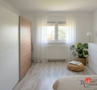 Světlá ložnice ve 4-pokojovém bytě s minimalistickým nábytkem a podlahou s dřevěným dekorem.