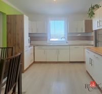 Kuchyně ve 4-pokojovém bytě s bílými skříněmi a dřevěným dekorem na podlaze.