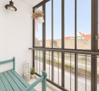 Zasklený balkon 2pokojového bytu s lavičkou, rostlinou a výhledem na městskou ulici.
