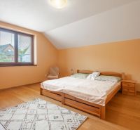 Ložnice s podlahou s dřevěným dekorem v rodinném domě, světlý nábytek a okno s výhledem.