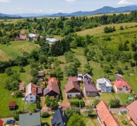 Pohled na rodinné domy v Horní Lhotě s kopcovitou krajinou v pozadí.