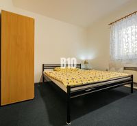 Ložnice v rodinném domě s kovovou postelí, skříní a vzorovanou záclonou.