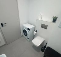Koupelna s pračkou, toaletou a béžovou dlažbou v 2-pokojovém bytě.