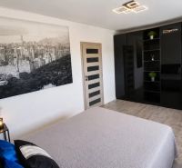 Ložnice s černou šatní skříní, velkou fotografií a pokojovými rostlinami.