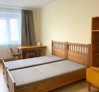 Ložnice s dřevěnými postelemi, stolem a podlahou s dřevěným dekorem v třípokojovém bytě.