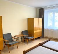 Pokoj v 3-pokojovém bytě s podlahou s dřevěným dekorem, dvě křesla a skříň.
