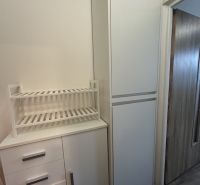 Garsonka s bílými skříňkami a regálem na tmavé podlaze s dřevěným dekorem.