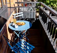Balkon 2-pokojového bytu s modrým stolem a židlemi, dřevěná podlaha, pevné zábradlí.