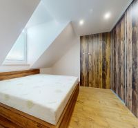 Ložnice se šikmým stropem, vestavěnou skříní a podlahou s dřevěným dekorem ve 4pokojovém bytě.