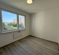 Pokoj v 3-pokojovém bytě s podlahou s dřevěným dekorem a velkými okny.