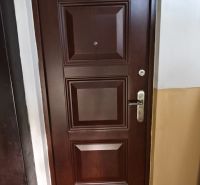 Vchodové dveře do 1-pokojového bytu s dřevěným dekorem a kováním.