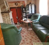 Interiér chaty s krbem, koženou sedací soupravou a vitrínou na podlaze s dřevěným dekorem.
