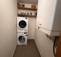 Prádelna v 3-pokojovém bytě s pračkou, sušičkou, policemi a plynovým kotlem.