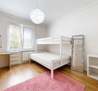 Dětský pokoj ve 3-pokojovém bytě s palandou, žlutou židlí, regály a podlahou s dřevěným dekorem.