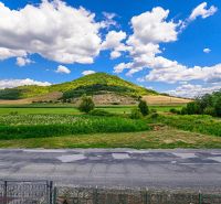 Krajina u rodinného domu v Hajnáčce, louky a kopce pod modrou oblohou.