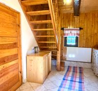 Interiér rodinného domu s dřevěným schodištěm, stropem a dveřmi, dlažba na podlaze.