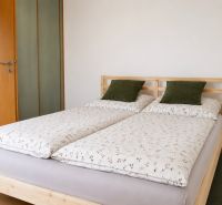 Ložnice s manželskou postelí, polštáři v 2-pokojovém bytě na podlaze s dřevěným dekorem.