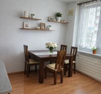 Jídelní kout se stolem, židlemi a poličkami na podlaze s dřevěným dekorem ve 3-pokojovém bytě.