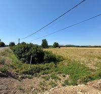 Pozemky na bydlení v Hokovcích, vedle cesty, s elektrickými vedeními nad nimi.