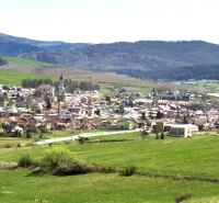 Ľubica obklopená zemědělskými a lesními pozemky s kopci v pozadí.