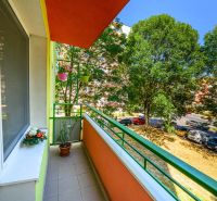 Balkon 2-pokojového bytu na Sládkovičově ulici ve Fiľakovu, lemovaný zelení, s květinami.