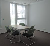 Kanceláře s kobercovou podlahou, konferenční stolek, zelené židle, přirozené světlo.