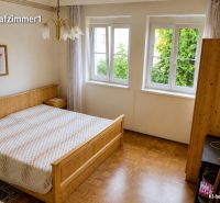 Ložnice v rodinném domě s podlahou s dřevěným dekorem, velkým oknem a postelí.