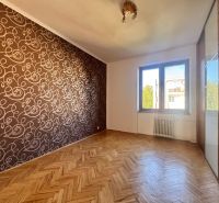 Pokoj ve 4pokojovém bytě s podlahou s dřevěným dekorem a vzorovanou tapetou.