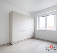 Světlý pokoj s bílou skříní a podlahou s dřevěným dekorem ve 3-pokojovém bytě.