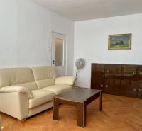 Obývací pokoj s krémovou sedačkou, dřevěným stolkem a skříňkou na podlaze s dřevěným dekorem.