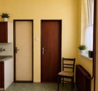 Kuchyně v rodinném domě se žlutými stěnami, tmavě hnědými dveřmi a radiátorem.