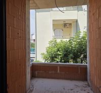 Nedokončený balkon v 3-pokojovém bytě s výhledem na zeleň a sousední budovu.